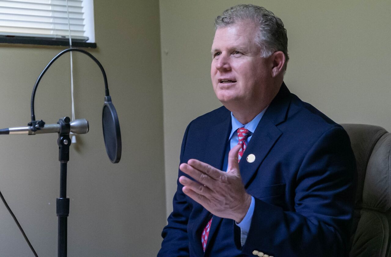 Bill Feehan seated at a microphone, speaking while recording a podcast episode in a studio setting